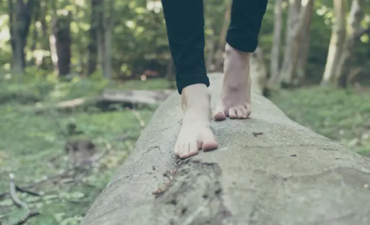 Riflessologia plantare, immagine di donna a piedi nudi che cammina su tronco di albero orizzontale sulla terra